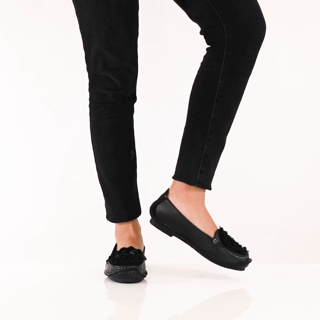 L'Artiste Dezi Black flats worn with black trousers; still from manufacturer product video, original studio background