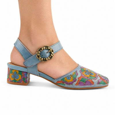 AI-generated on-model styling view of L'Artiste Funferbiz Blue Multi: powder-blue floral closed-toe shoe with blue straps, scalloped brass-tone buckle and low floral block heel on white.
