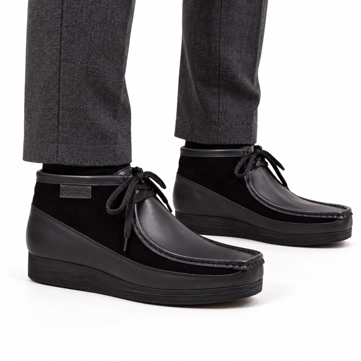 AI-generated on-model view of British Walkers New Castle Classic black leather-and-suede ankle boots with charcoal trousers on a white background.
