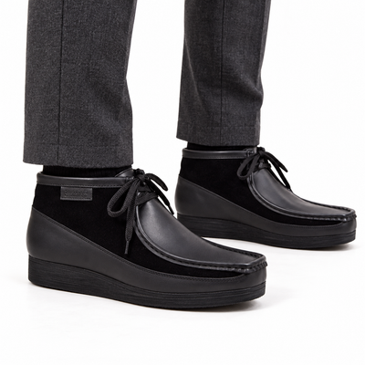 AI-generated on-model view of British Walkers New Castle Classic black leather-and-suede ankle boots with charcoal trousers on a white background.