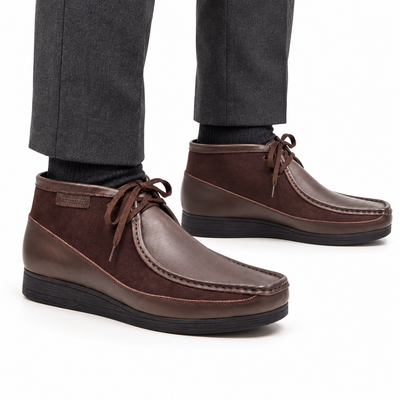 AI-generated on-model view of British Walkers New Castle Classic dark brown leather-and-suede ankle boots with charcoal trousers on a white background.