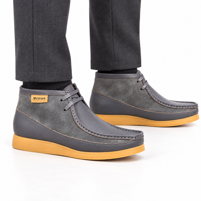 AI-generated on-model view of British Walkers New Castle Classic gray leather-and-suede ankle boots with tan soles and charcoal trousers on a white background.