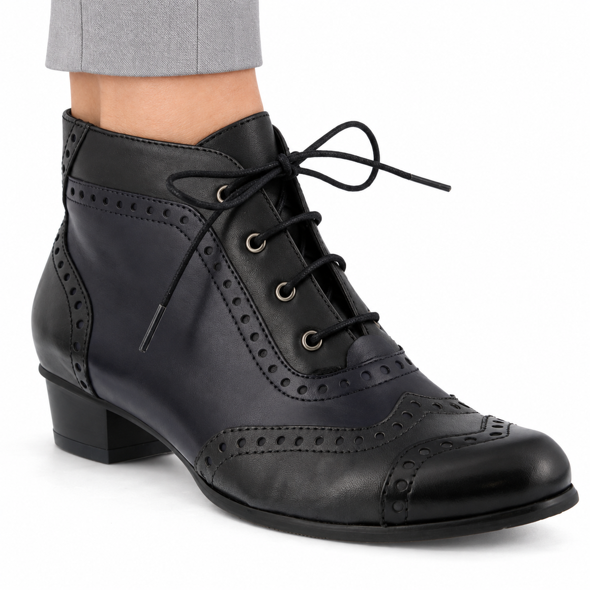 AI-generated on-model view of the Spring Step Heroic women's Black ankle boot with subtle dark navy panels, brogue detailing and black laces, worn with light gray trousers on a white background.